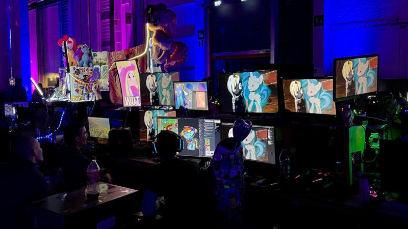 A section of the Assembly event floor in Helsinki, showing rows of gaming setups with multiple monitors displaying animated characters and digital art. Some setups are uniquely decorated, reflecting the creative and individual expression within the large gaming community that Hive Helsinki students are part of.