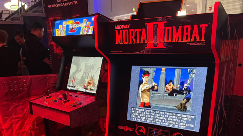 Two classic arcade machines, "Mortal Kombat II" and "Marvel vs. Capcom 2," are prominently displayed at the Assembly event in Helsinki. The screens show iconic fighting game characters, appealing to both nostalgic gamers and those exploring the history of video games, a common interest among Hive Helsinki students.