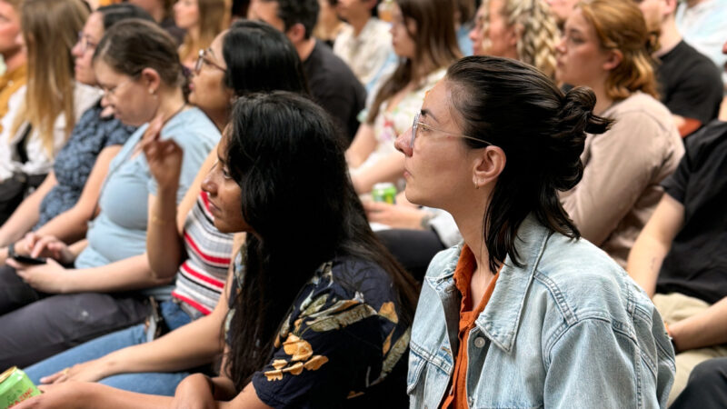 A close-up of a diverse audience at a Hive Helsinki event, with individuals seated and attentively listening to a presentation. The focus is on two young women in the foreground, showcasing the engaged community present at tech education and networking events in Helsinki, Finland.