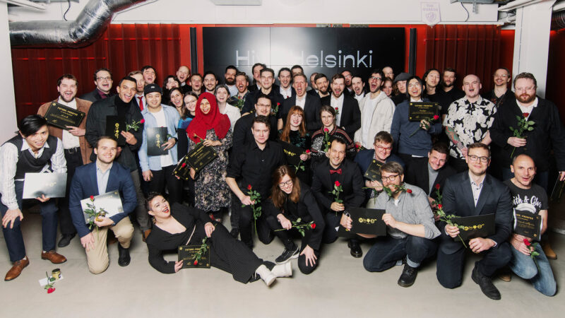 A large, celebratory group of Hive Helsinki graduates posing together for a class photo. They are holding diplomas or certificates and red roses, with many smiling and some making excited gestures, highlighting the successful completion of their coding education and their readiness for future tech careers in Helsinki, Finland.