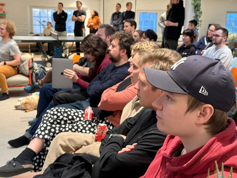 A diverse audience of Hive Helsinki students and community members attentively listening to a presentation at a Demoday event. People are seated on chairs and couches, demonstrating the engaging peer-to-peer learning and networking opportunities available at the coding school in Helsinki, Finland.