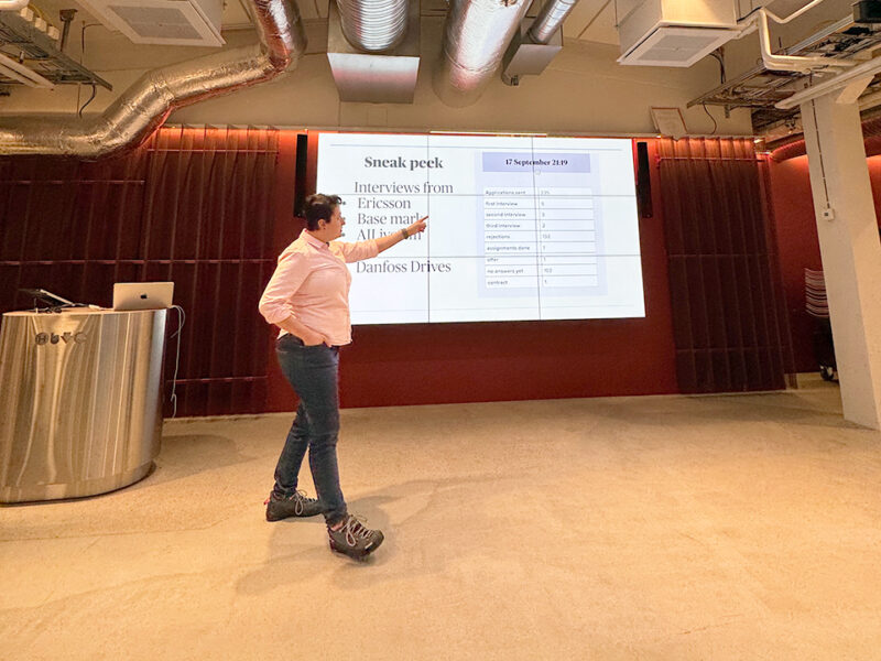 A speaker presents "Job hunting for realists" to an audience in a modern event space in Hive Helsinki. The speaker is pointing to the screen.
