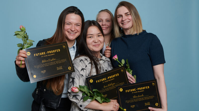 Four smiling female graduates of Hive Helsinki proudly holding their "FUTURE-PROOFED AT HIVE HELSINKI" certificates and pink roses. This image celebrates the success of women in tech education and their readiness for futureproofing careers after completing their innovative coding program in Helsinki, Finland.