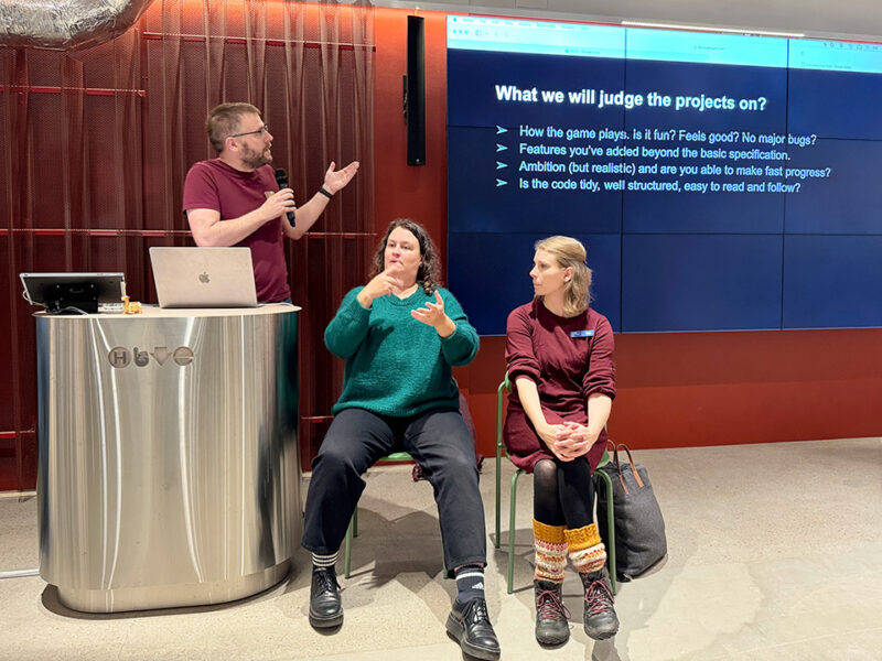 Speakers at the Supercell Challenge 2024 at Hive Helsinki explain the criteria for judging projects. The screen lists points like "How the game plays," "Features you've added," and "Is the code tidy, well structured." This demonstrates the focus on practical application, problem-solving, and high-quality coding standards in Hive Helsinki's tech education in Finland.