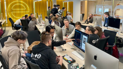 A busy and collaborative coding lab at Hive Helsinki during the Winter Piscine 2024. Students are actively working on Apple iMac computers, with many engaged in peer-to-peer learning and discussions. This dynamic environment showcases the hands-on approach to tech education in Helsinki, Finland.