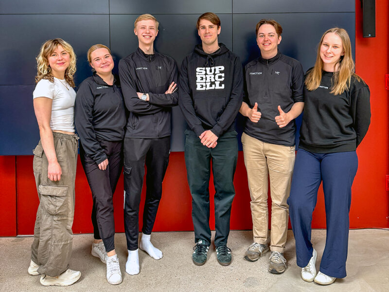 The Hive Helsinki, Junction and Supercell team responsible for organizing the Supercell AI Hackathon at Hive Helsinki. A group of six young adults, two women and four men, standing together and smiling at the camera. Most are wearing dark athletic wear with "JUNCTION" branding, and one person is wearing a "SUPERCELL" hoodie.