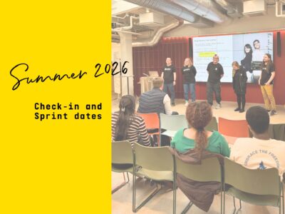 Hive Helsinki team standing at the front of a room during a check-in event, with attendees seated and a screen visible in the background.